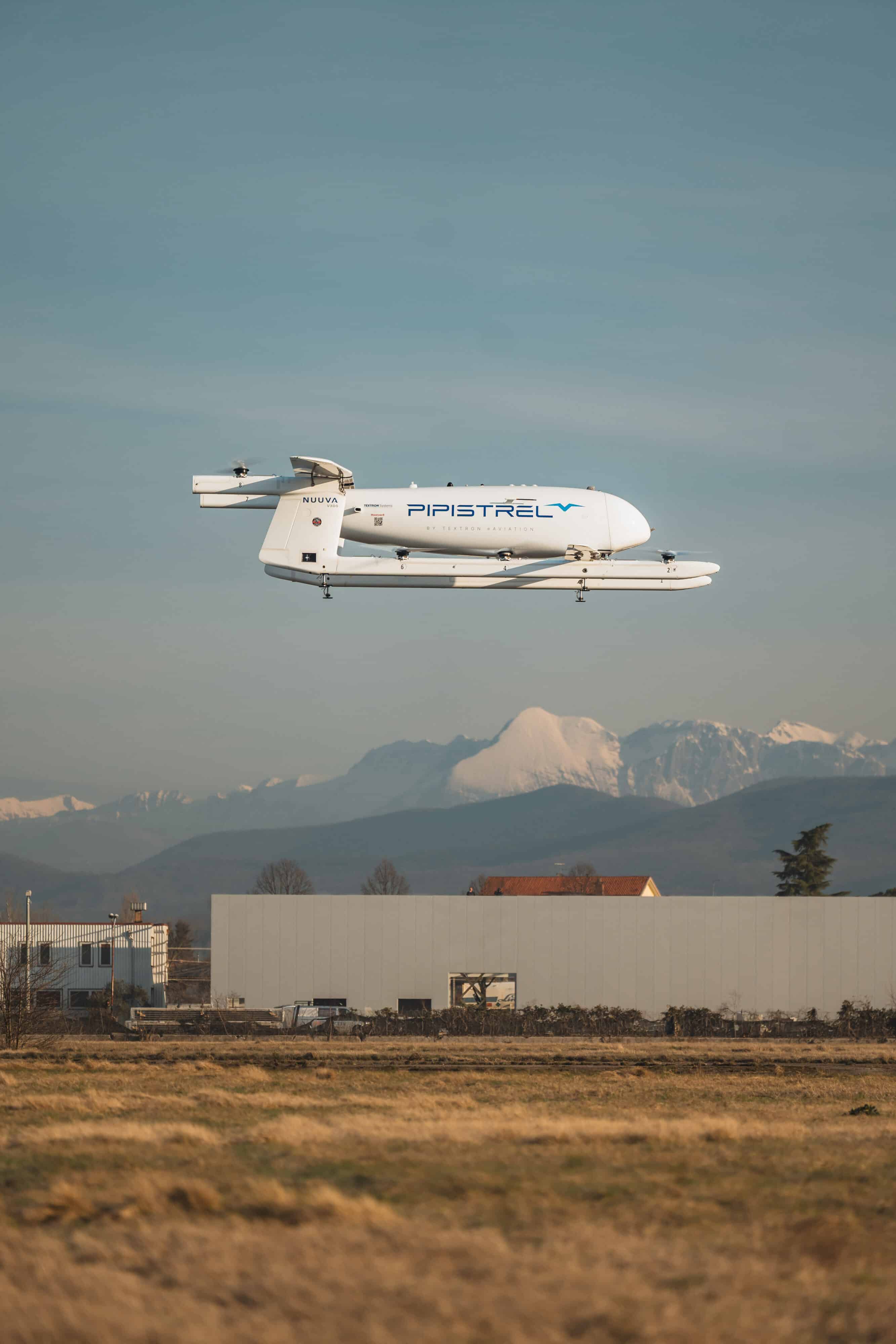 Nuuva hovering above field with buildings and mountains in background
